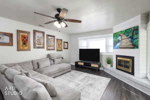 Living area featuring a textured ceiling, dark wood finished floors, a fireplace, and ceiling fan