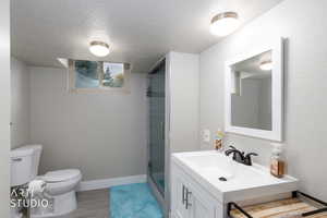 Bathroom featuring a textured ceiling, vanity, a stall shower, and light wood finished floors