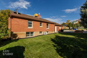 Rear view of property with a yard, a chimney, and brick siding