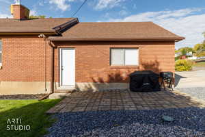 Rear view of house with a patio, roof with shingles, brick siding, and a chimney