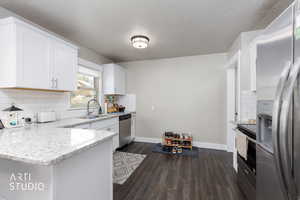 Kitchen with tasteful backsplash, appliances with stainless steel finishes, dark wood-type flooring, a peninsula, and light stone counters