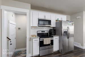 Kitchen with stainless steel appliances, backsplash, white cabinetry, dark wood finished floors, and light stone counters