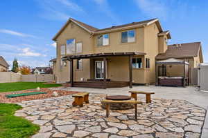 Rear view of property with a patio, a fenced backyard, a fire pit, stucco siding, and a hot tub