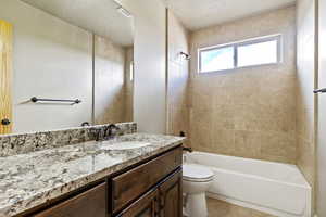 Bathroom with vanity, shower / bath combination, a textured ceiling, and light tile patterned flooring