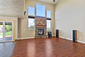 Unfurnished living room with a high ceiling, a stone fireplace, dark wood-style flooring, and ceiling fan