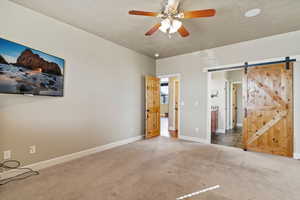 Unfurnished bedroom with a barn door, carpet, a textured ceiling, ceiling fan, and ensuite bathroom