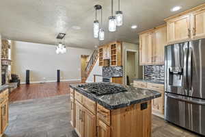 Kitchen with stainless steel fridge with ice dispenser, hanging light fixtures, a textured ceiling, backsplash, and a stone fireplace