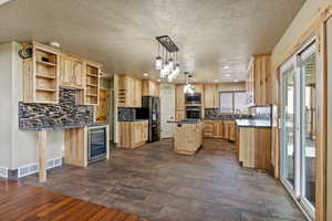 Kitchen with light brown cabinets, dark wood-style flooring, decorative light fixtures, backsplash, and beverage cooler