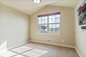 Spare room featuring light colored carpet and lofted ceiling