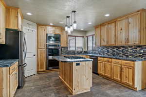 Kitchen featuring dark countertops, a textured ceiling, pendant lighting, stainless steel appliances, and a kitchen island