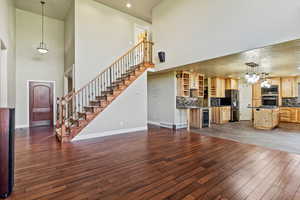 Unfurnished living room with a towering ceiling, dark wood-type flooring, stairs, beverage cooler, and recessed lighting