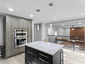 Kitchen with hanging light fixtures, a kitchen island, light wood-style floors, stainless steel double oven, and dark cabinetry