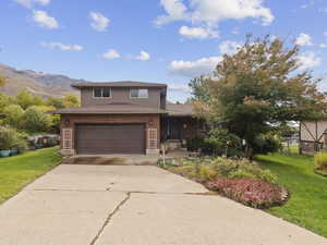 Traditional home with a front yard, concrete driveway, brick siding, a garage, and roof with shingles