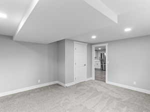 Finished basement with light colored carpet, recessed lighting, and stainless steel fridge with ice dispenser