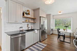 Kitchen with dark countertops, backsplash, stainless steel appliances, open shelves, and dark wood-style floors