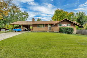Ranch-style home featuring brick siding, a chimney, an attached carport, and driveway