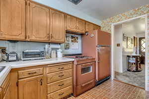 Kitchen with electric range oven, light countertops, brick patterned floors, freestanding refrigerator, and backsplash