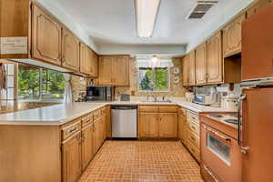 Kitchen featuring freestanding refrigerator, stainless steel dishwasher, a peninsula, light countertops, and range with electric stovetop
