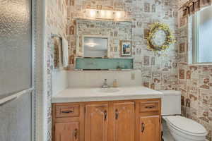 Primary bedroom bathroom with vanity and wallpapered walls. Shower to left.