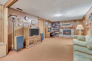 Carpeted living area with wood walls, an office area, and a brick fireplace