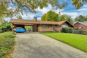 Ranch-style house with a chimney, brick siding, a carport, a front lawn, and driveway