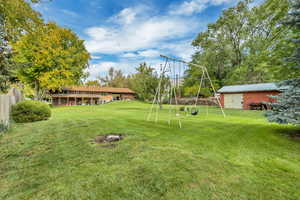 View of grassy yard with an house, swingset and workshop/shed in distance.