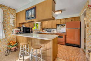 Kitchen featuring wallpapered walls, a kitchen breakfast bar, light countertops, freestanding refrigerator, and a peninsula