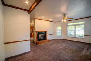 Unfurnished living room with crown molding, a fireplace, dark colored carpet, a ceiling fan, and beamed ceiling