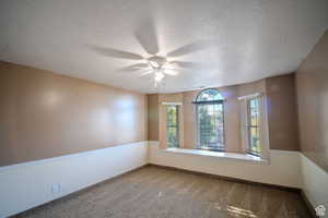 Empty room featuring carpet flooring, a textured ceiling, and ceiling fan