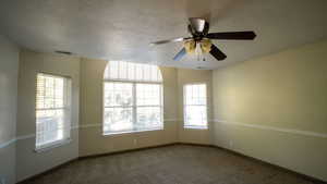 Empty room featuring a textured ceiling, carpet flooring, and a ceiling fan