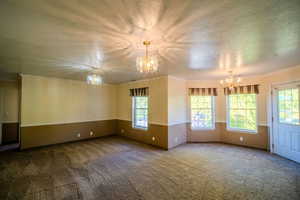 Spare room featuring a chandelier, crown molding, carpet, and a textured ceiling