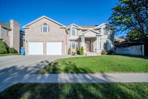 Traditional-style home featuring a front lawn, concrete driveway, brick siding, and a garage