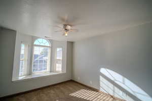 Carpeted empty room with ceiling fan and a textured ceiling