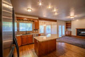 Kitchen featuring appliances with stainless steel finishes, brown cabinetry, a textured ceiling, light stone counters, and decorative backsplash