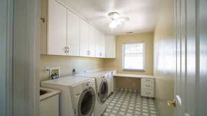 Laundry area with washing machine and dryer, a ceiling fan, light floors, cabinet space, and a textured ceiling