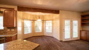 Kitchen featuring brown cabinetry, open shelves, backsplash, carpet, and beamed ceiling