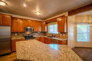 Kitchen featuring stainless steel appliances, brown cabinetry, tasteful backsplash, light stone countertops, and a textured ceiling