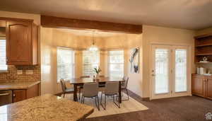 Dining space with beam ceiling, healthy amount of natural light, light colored carpet, and a chandelier