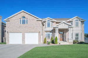 View of front of property featuring a front lawn, an attached garage, concrete driveway, and brick siding