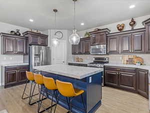 Kitchen featuring tasteful backsplash, a kitchen bar, dark brown cabinetry, appliances with stainless steel finishes, and decorative light fixtures