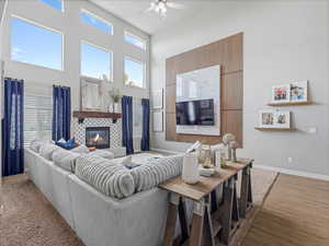 Living room with a high ceiling, a tiled fireplace, a ceiling fan, and wood finished floors