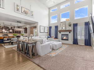 Living room with a tiled fireplace, healthy amount of natural light, a high ceiling, light carpet, and ceiling fan