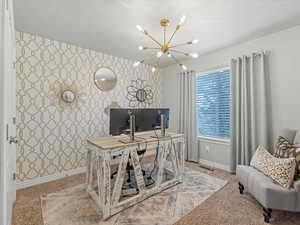 Home office featuring wallpapered walls, carpet, a chandelier, and an accent wall