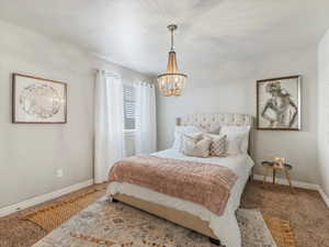 Carpeted bedroom with baseboards and a chandelier
