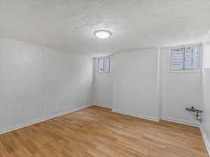 Basement with light wood-style flooring and a textured ceiling