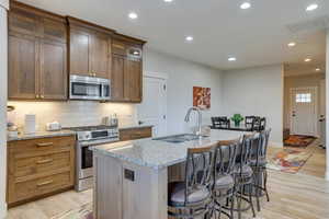 Kitchen with backsplash, light stone counters, appliances with stainless steel finishes, light wood-style flooring, and recessed lighting