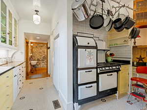 Kitchen featuring glass insert cabinets, decorative backsplash, black gas range, dark countertops, and freestanding refrigerator