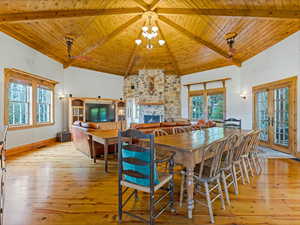 Dining room with high vaulted ceiling, a wooden ceiling with exposed beams, a stone fireplace, light wood-type flooring, and a chandelier
