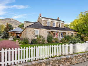 View of front facade with stone siding, a chimney, a gazebo, covered porch, and a fenced front yard