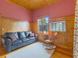 Living room with wooden ceiling, light wood finished floors, wood walls, and a wainscoted wall